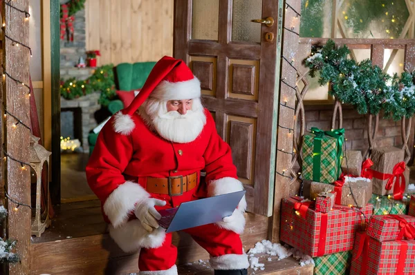 Santa Claus sedí na verandě domu a používá laptop. Vánoční koncept — Stock fotografie