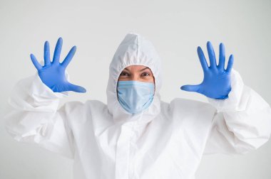 Koruyucu giysili bir kadın ve korkunç bir buruşukluğu olan tıbbi bir maske. Doktor avuçlarını yüzüne dayadı ve korktu.