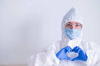 Koruyucu kıyafetli kadın doktor kalbi bir jestle gösteriyor. Hasta sağlığı konsepti