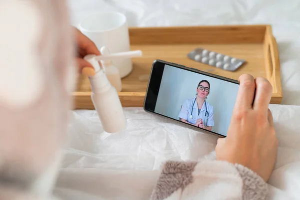 Una mujer se encuentra en casa en la cama y consulta en un teléfono inteligente. Medicina en línea — Foto de Stock