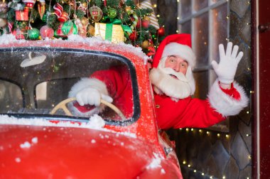 Kırmızı bir retro araba kullanırken Noel Baba selamlıyor. Mutlu Noeller.