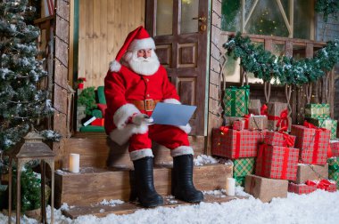 Noel Baba evin verandasında oturuyor ve bir dizüstü bilgisayar kullanıyor. Noel konsepti