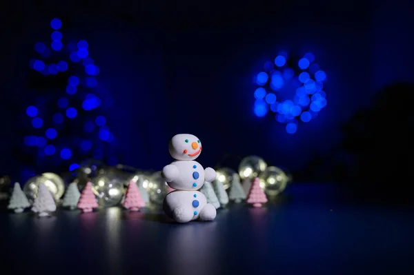 Cute snowman and little Christmas trees made of marshmallows on the background of Christmas lights. Garland of light bulbs on a tree. Happy new year. — Stock Photo, Image