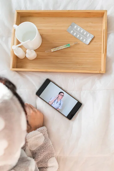 一个女人躺在家里的床上，用智能手机进行咨询。网上药物 — 图库照片