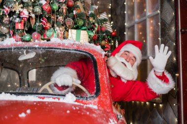 Kırmızı bir retro araba kullanırken Noel Baba selamlıyor. Mutlu Noeller.