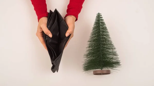 Uma mulher está segurando uma bolsa vazia ao lado de uma pequena árvore de Natal artificial. A crise financeira durante os feriados — Fotografia de Stock