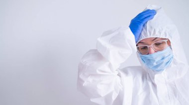 Koruyucu kıyafetli ve tıbbi maskeli bir kadın kafasını tutuyor. İşte sorunları olan bir doktor virüs uzmanı.