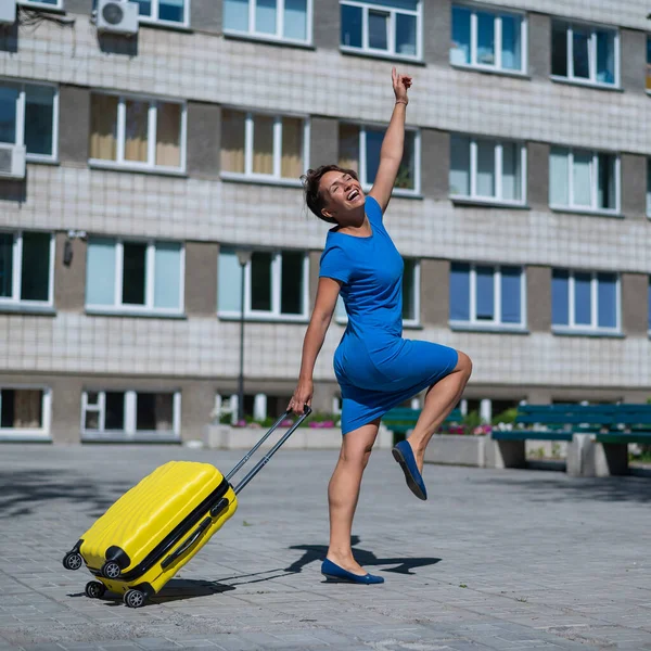 Gelukkige vrouw loopt door de straat met gele koffer met wielen — Stockfoto