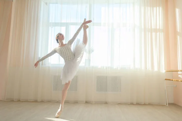 Bela bailarina em corpo e tutu branco está treinando em uma aula de dança. Jovem dançarina flexível posando em sapatos pontiagudos. — Fotografia de Stock