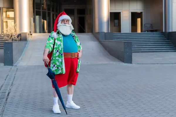 Le Père Noël vêtu d'un short se promène en ville avec un parapluie — Photo