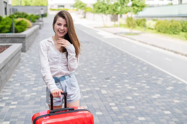 Een mooie blanke vrouw loopt door de straat met een grote bagage op wielen. Het meisje gaat op vakantie. — Stockfoto