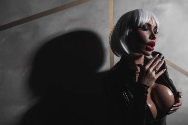 Sexy woman in a blonde wig and latex catsuit. Girl with big fake tits