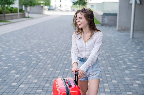Schöne kaukasische Frau geht mit rotem Koffer auf eine Reise und wartet auf ein Taxi. — Stockfoto