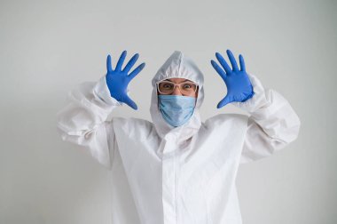 Koruyucu giysili bir kadın ve korkunç bir buruşukluğu olan tıbbi bir maske. Doktor avuçlarını yüzüne dayadı ve korktu.
