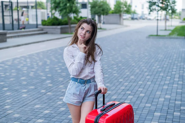 Mooie blanke vrouw gaat op reis met een rode koffer en wacht op een taxi. — Stockfoto