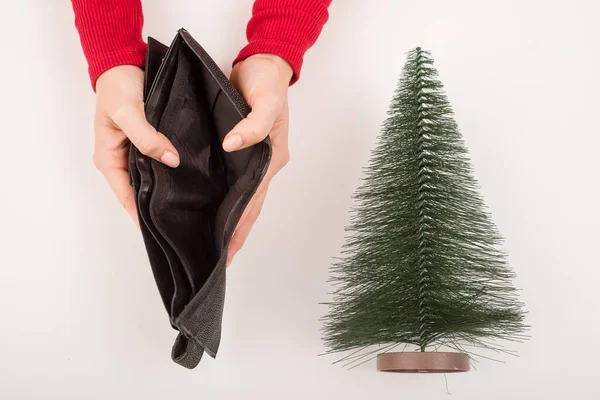 Egy nő egy üres pénztárcát tart egy kis mesterséges karácsonyfa mellett. A pénzügyi válság az ünnepek alatt — Stock Fotó
