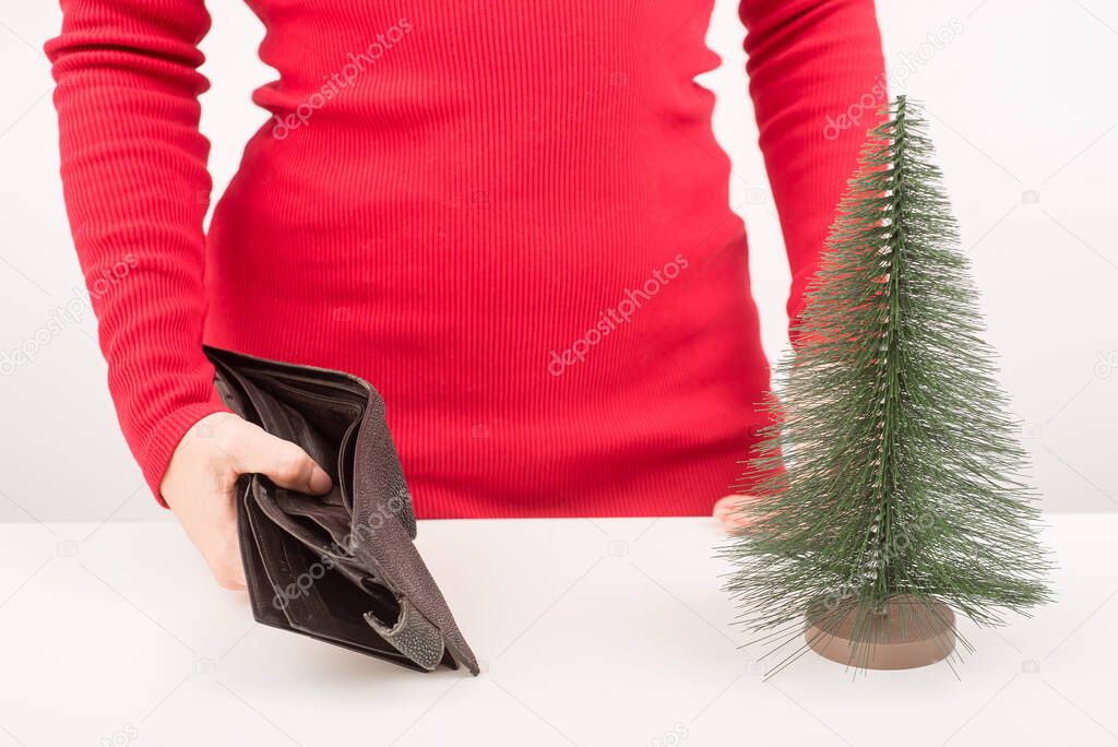 A woman is holding an empty purse next to a small artificial Christmas tree. The financial crisis during the holidays
