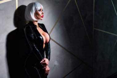 Sexy woman in a blonde wig and latex catsuit. Girl with big fake tits