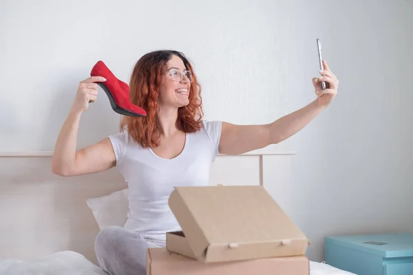 Mujer caucásica sentada en la cama y tomando una selfie con una compra de parto. Compras online de zapatos — Foto de Stock