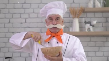 Yaşlı bir erkek şef ahşap bir kasede yumurta çırpar. Mutfakta çalışan yaşlı adam..
