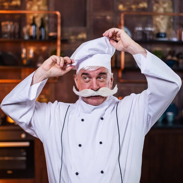 Un vieux chef masculin ajuste son chapeau dans la cuisine — Photo