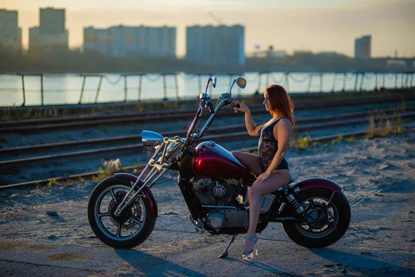 Mujer pelirroja en lencería sexy en tacones altos se sienta en una motocicleta. Atractiva chica pelirroja se sienta en una motocicleta al atardecer — Foto de Stock
