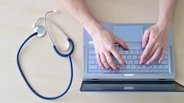 Klavyedeki ellerin üst görüntüsü. Masada dizüstü bilgisayarda yazan kadın doktor. Hemşire hastalara elektronik kart doldurur..