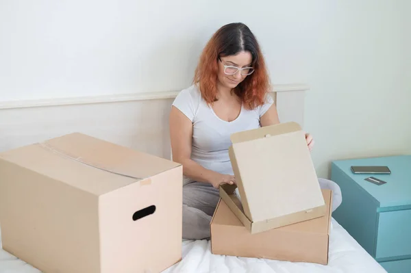 Caucasian woman opens an order while sitting in bed. Online shopping concept with home delivery — Stock Photo, Image