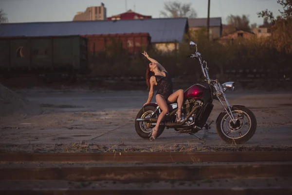 Schöne sexy Frau in Spitzenbody und High Heels sitzt auf einem Motorrad auf einem industriellen Hintergrund — Stockfoto