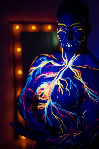 UV μοτίβα σώματος τέχνης του κυκλοφορικού συστήματος σε ένα ανθρώπινο σώμα. Στον κορμό ενός μυϊκού αθλητή, φλέβες και αρτηρίες έλκονται με φθορίζουσες βαφές. Bodybuilder στέκεται δίπλα στον καθρέφτη με λαμπτήρες. — Φωτογραφία Αρχείου