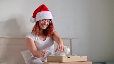 Hüsrana uğramış, Noel Baba şapkalı, beyaz bir kediyle yatakta oturan beyaz bir kadın kutuyu açar ve yanlış sipariş alır.