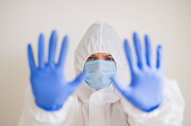Koruyucu giysili, tıbbi maskeli ve lateks eldivenli bir kadın, dur hareketi gösteriyor. Koronavirüs salgınında yorgun doktor