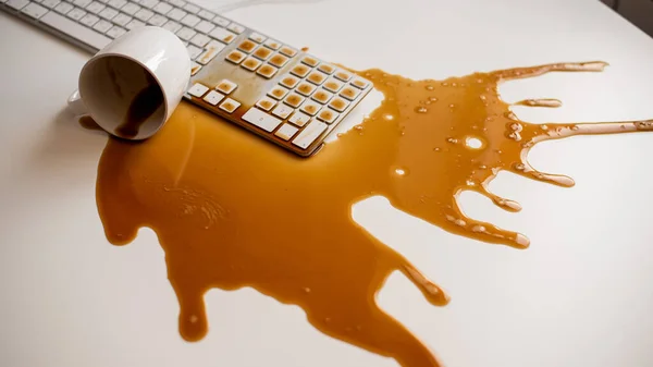 Café preto derramado em um teclado de computador em uma mesa branca — Fotografia de Stock