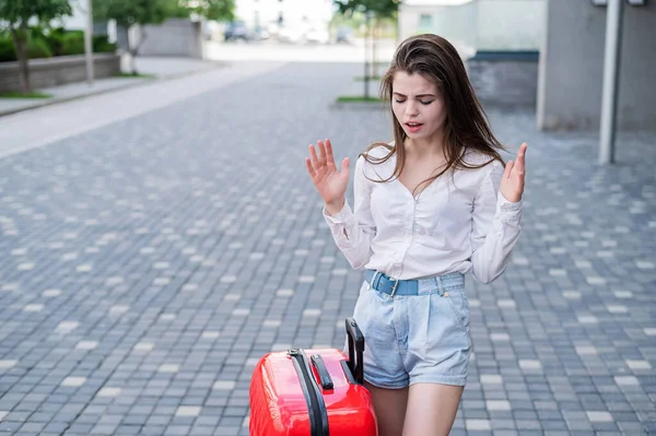 Mooie blanke vrouw gaat op reis met een rode koffer en wacht op een taxi. — Stockfoto