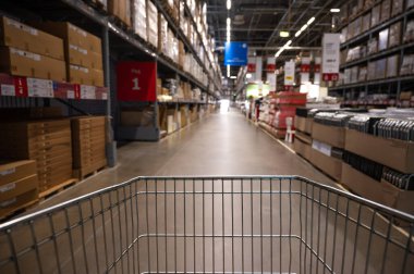 Mobilya deposunda boş bir alışveriş arabası. Kutu rafı soyut bulanık arka planla süpermarket alışveriş sepeti koridoru
