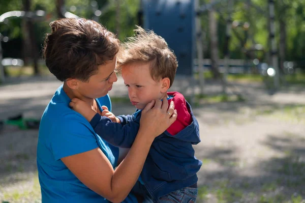 Kadın çocuk parkında oğluna nazikçe sarılıyor. Küçük çocuk yaramazdır ve annesi onu sakinleştirir. — Stok fotoğraf