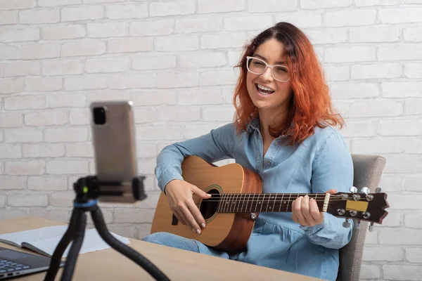 Een vrouw zendt online uit op haar telefoon thuis. Het meisje zingt en speelt de gitaar live — Stockfoto