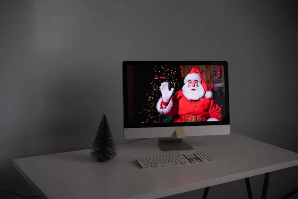 Papai Noel deseja remotamente Feliz Natal através de uma chamada de vídeo no computador. Um homem vestido de Pai Natal num monitor. 2021 conceito de ano novo — Fotografia de Stock