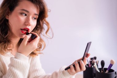 Kadın dudaklarına ruj sürer ve cep aynasına bakar..