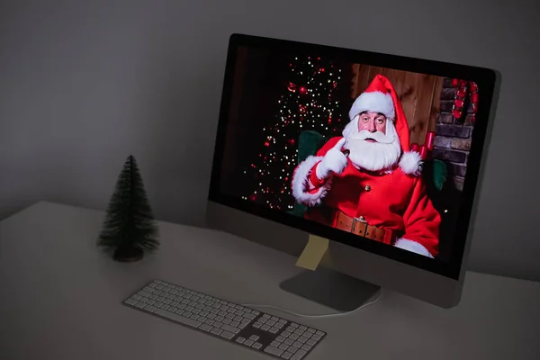 Święty Mikołaj zdalnie życzy Wesołych Świąt za pośrednictwem połączenia wideo na komputerze. Mężczyzna przebrany za Świętego Mikołaja na monitorze. Koncepcja nowego roku 2021 — Zdjęcie stockowe