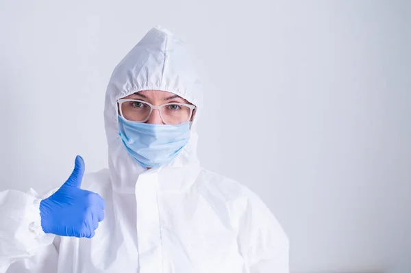 A woman in a protective suit and a medical mask shows a thumb up on a white background — Stock Photo, Image