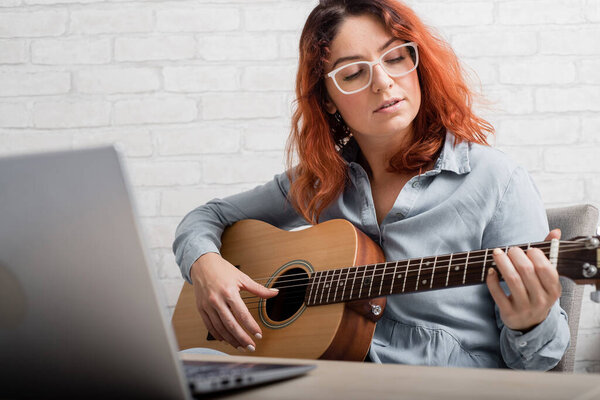 Caucasian woman learning to play guitar online. The girl sits in quarantine remotely studying music