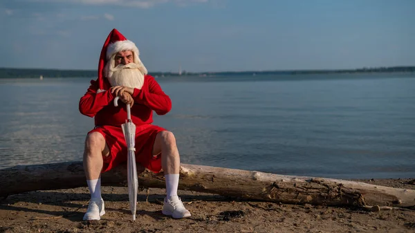 Santa Claus camina por la playa con un paraguas. Navidad en un país caliente —  Fotos de Stock