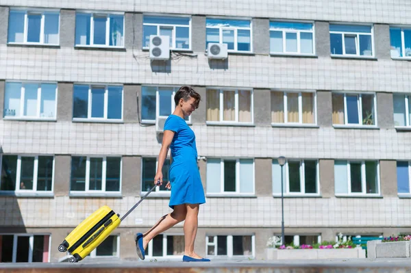 Glückliche Frau läuft mit gelbem Koffer mit Rädern die Straße entlang — Stockfoto