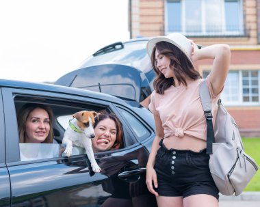 Mutlu üç kadın arabada oynaşıyor. Kız arkadaşlar köpekle araba ile seyahat ederler.