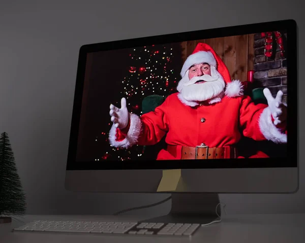 Papai Noel deseja remotamente Feliz Natal através de uma chamada de vídeo no computador. Um homem vestido de Pai Natal num monitor. 2021 conceito de ano novo — Fotografia de Stock