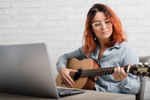 Fehér nő tanul gitározni online. A lány karanténban ül, zenét tanul. — Stock Fotó