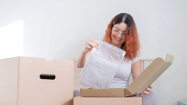 Caucasian woman opens an order while sitting in bed. Online shopping concept with home delivery — Stock Photo, Image