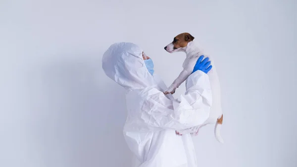 Жінка в захисному костюмі і масці тримає собаку-тер'єра Джека Рассела на білому тлі. — стокове фото