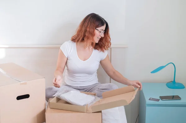 Caucasian woman opens an order while sitting in bed. Online shopping concept with home delivery — Stock Photo, Image